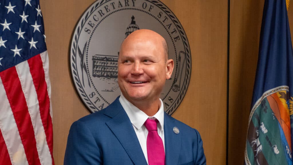 Kansas Secretary of State Scott Schwab smiles in front of the state seal and flags.