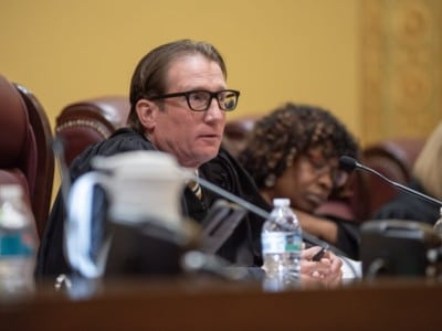 Missouri Supreme Court Chief Justice Brent Powell sits at the bench with a microphone and water bottle during a hearing.