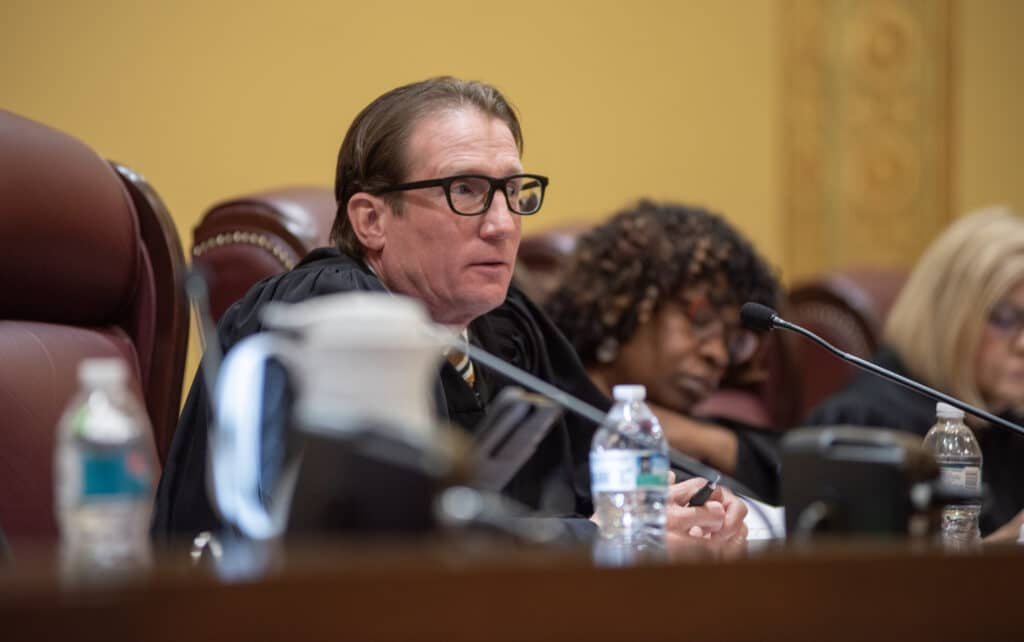 Missouri Supreme Court Chief Justice Brent Powell sits at the bench with a microphone and water bottle during a hearing.