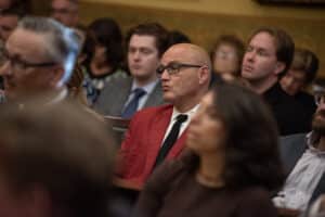 Missouri Secretary of State Denny Hoskins sits in a red suit jacket among an audience, looking forward attentively.