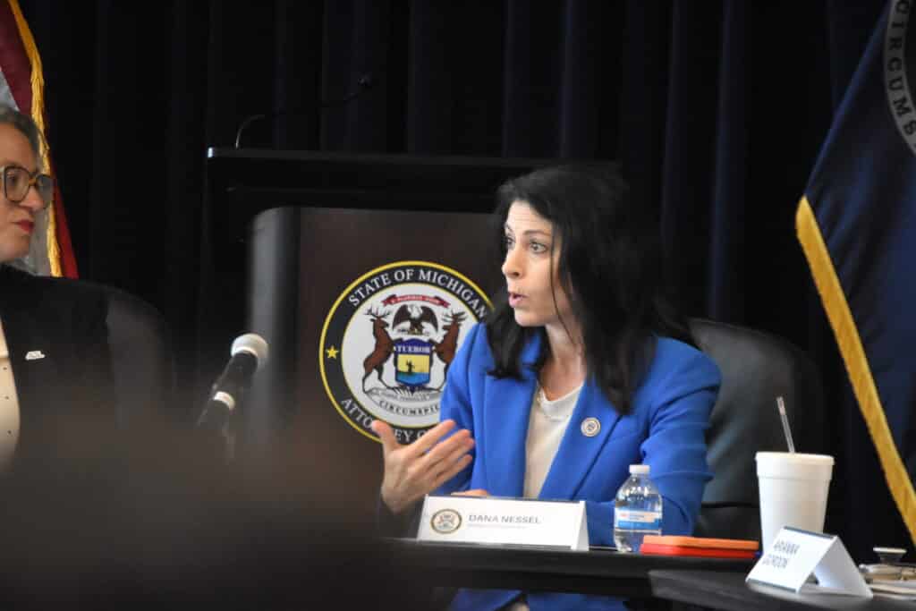 Michigan Attorney General Dana Nessel gestures with her hands while speaking at a press table.
