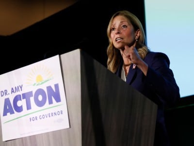 Dr. Amy Acton gestures while speaking at a podium bearing a sign that reads "DR. AMY ACTON FOR GOVERNOR."