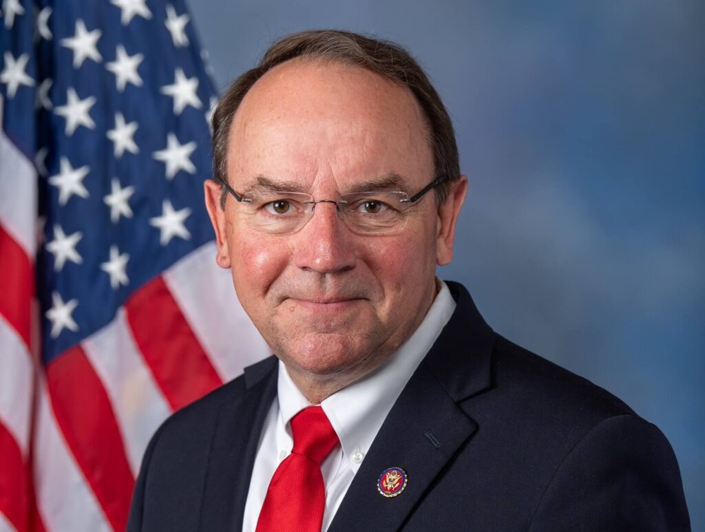 Official headshot of U.S. Rep. Tom Tiffany wearing a suit and red tie in front of an American flag.