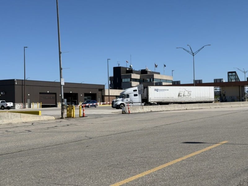 A semi-truck passes through the U.S. Customs station at the Blue Water Bridge under a clear blue sky.