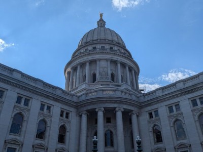 The white stone exterior dome and facade of the Wisconsin State Capitol building against a blue sky.