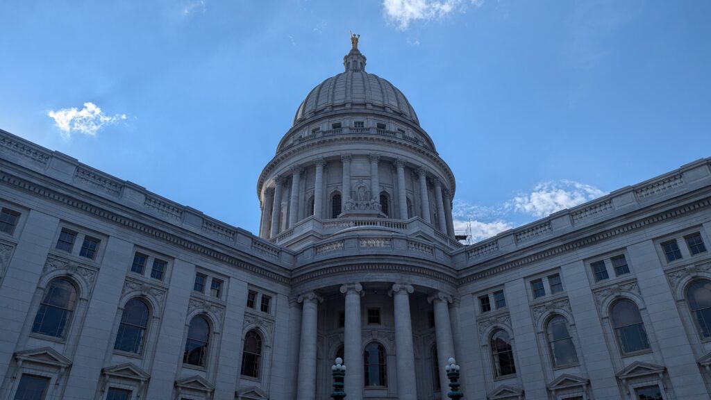 The white stone exterior dome and facade of the Wisconsin State Capitol building against a blue sky.