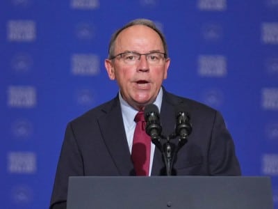 Rep. Tom Tiffany speaks into two microphones at a podium against a blue background.