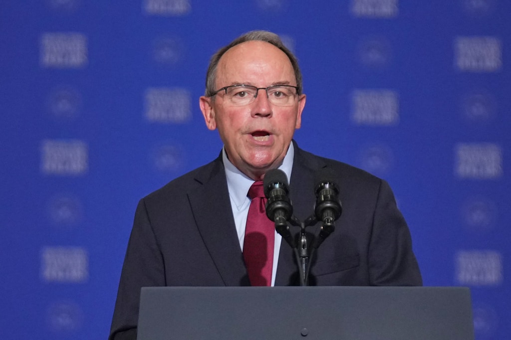 Rep. Tom Tiffany speaks into two microphones at a podium against a blue background.