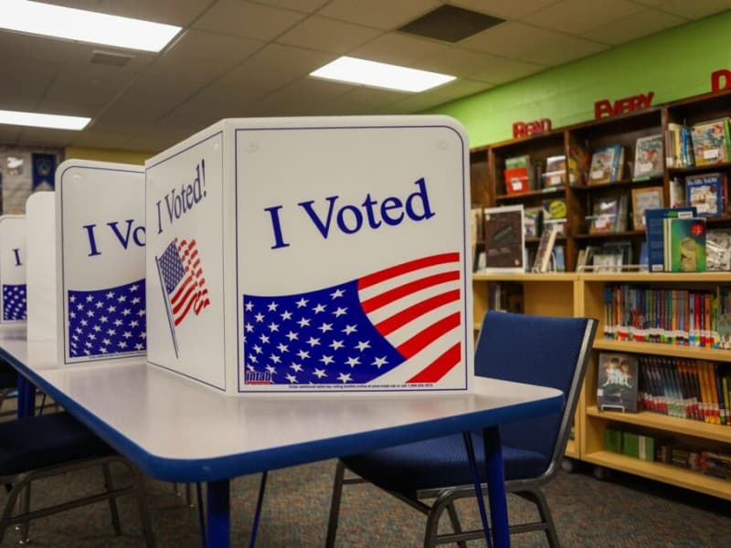 Tabletop voting booths printed with "I Voted" and American flag graphics set up inside a school library.