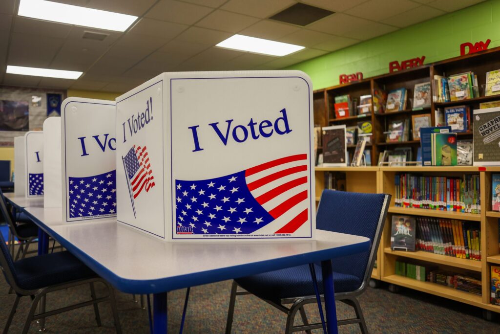 Tabletop voting booths printed with "I Voted" and American flag graphics set up inside a school library.