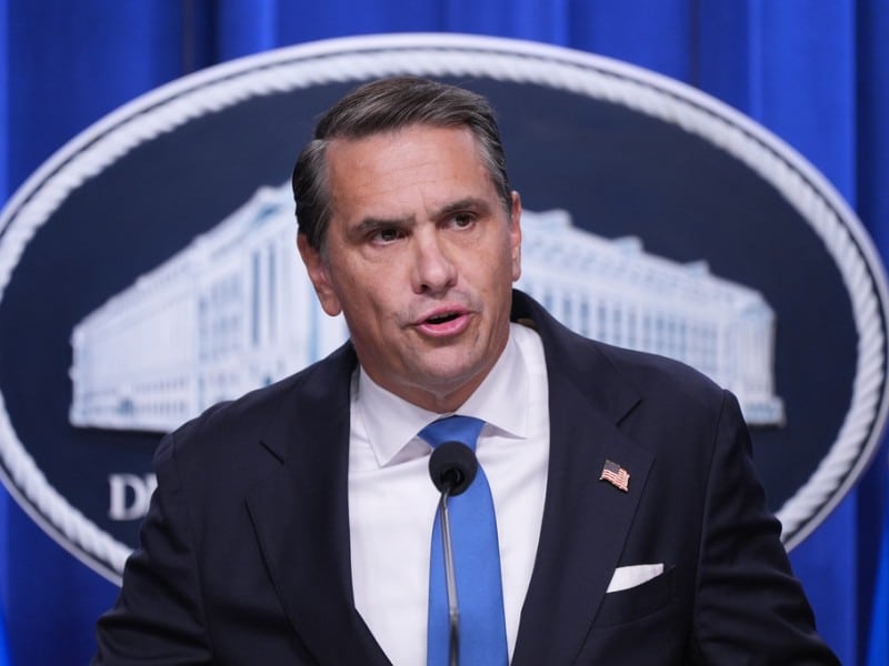 Todd Blanche speaks into a microphone at a podium in front of a Department of Justice seal.