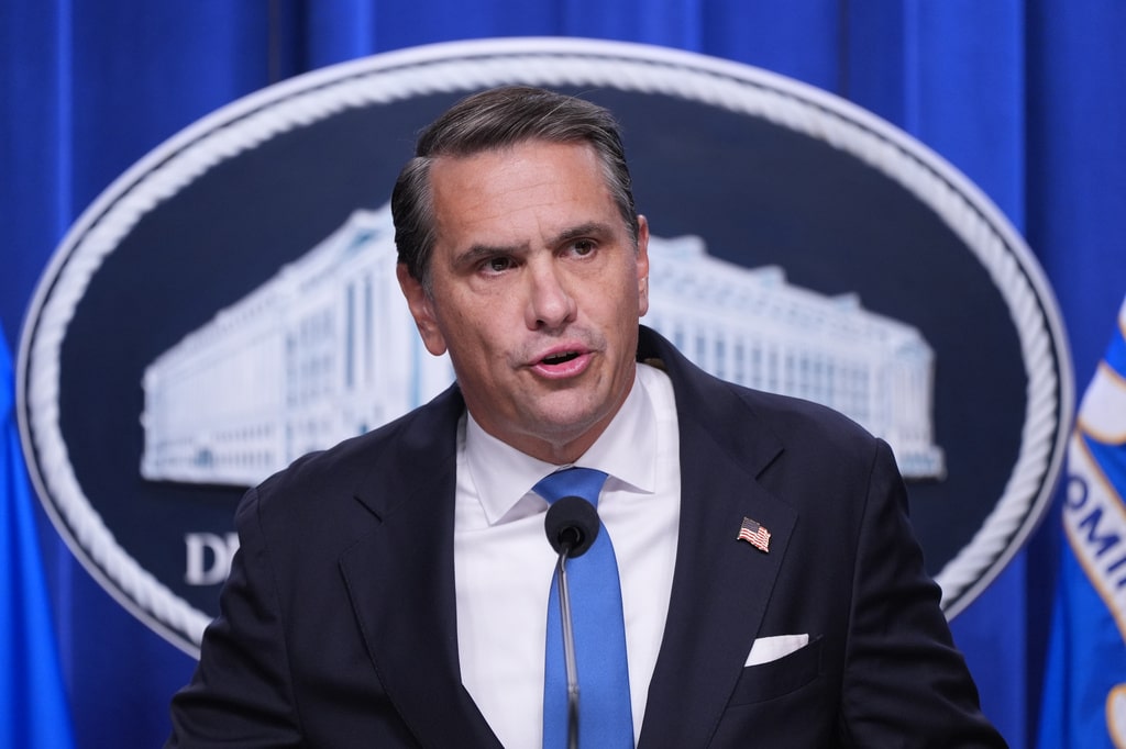 Todd Blanche speaks into a microphone at a podium in front of a Department of Justice seal.