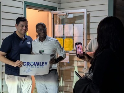 David Crowley and Soham Bhatnagar pose together holding a campaign sign as someone takes their picture with a smartphone.