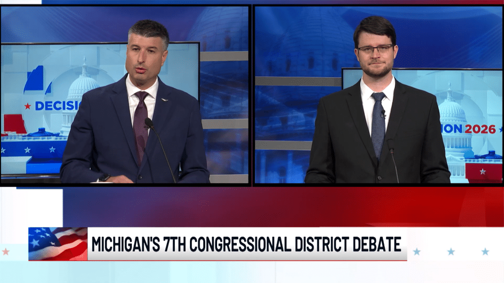 A split-screen news broadcast titled "MICHIGAN'S 7TH CONGRESSIONAL DISTRICT DEBATE" showing two men in suits at podiums.