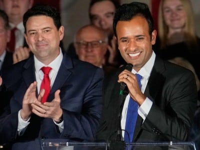 Vivek Ramaswamy speaks into a microphone while Rob McColley stands beside him clapping.