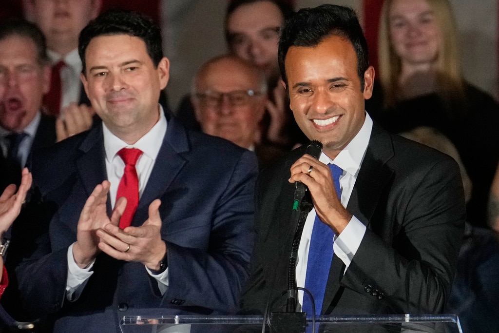 Vivek Ramaswamy speaks into a microphone while Rob McColley stands beside him clapping.