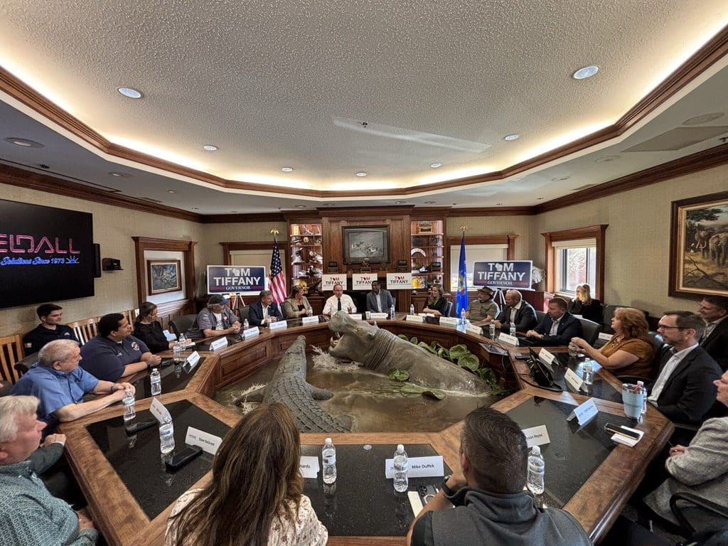 A campaign meeting around a large conference table with "Tom Tiffany Governor" signs and a life-size hippo and crocodile display in the center.