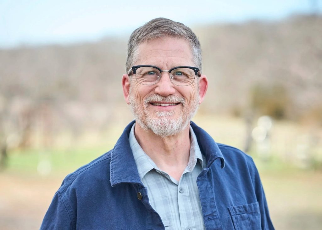 Headshot of Dan Kessler wearing glasses and smiling outdoors in a blue jacket.