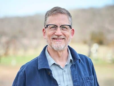 Headshot of Dan Kessler wearing glasses and smiling outdoors in a blue jacket.