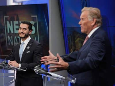 Mike Rogers gestures while speaking during a debate as Abdul El-Sayed looks on smiling.
